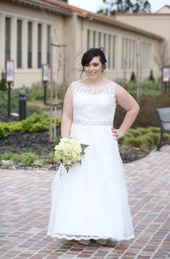 Brunette bride in white wedding dress with flowers at cobbled road