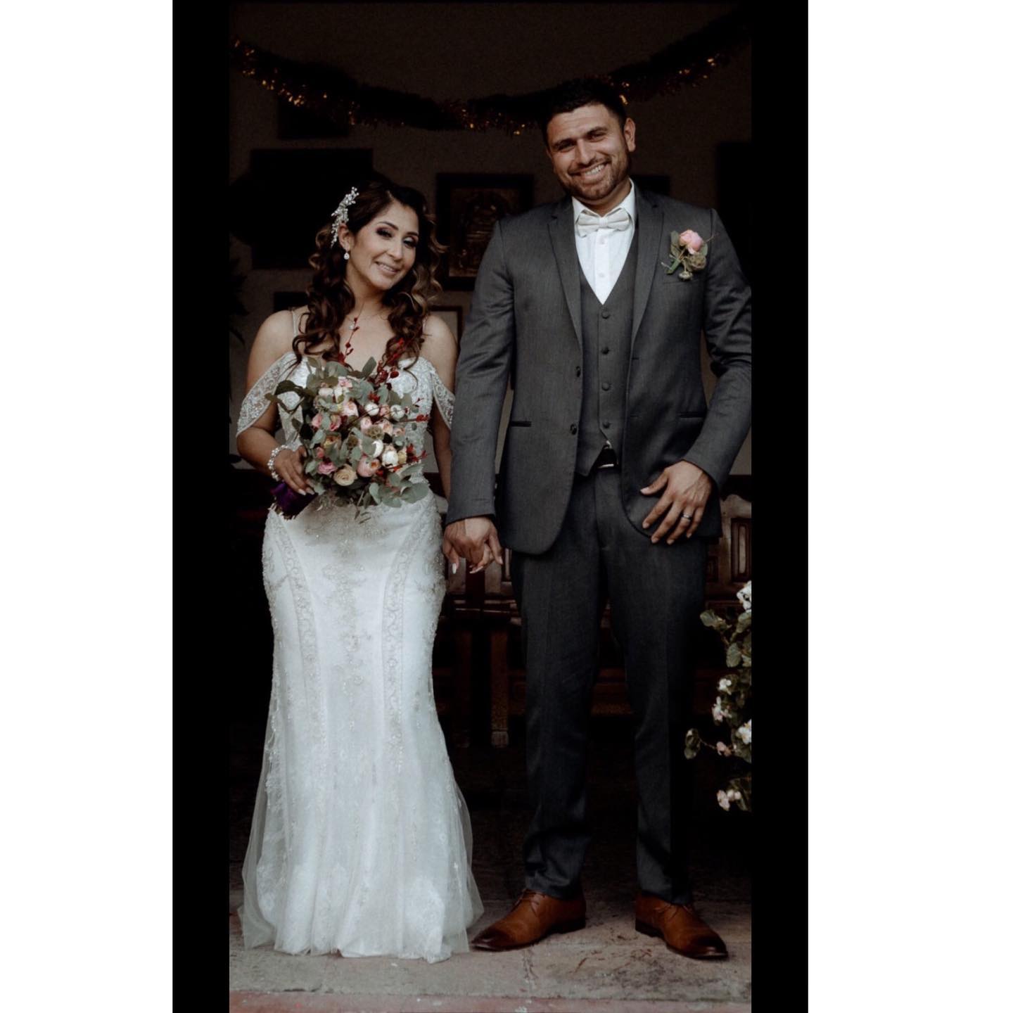 Brunette bride in white wedding dress with flowers is holding groom's hand