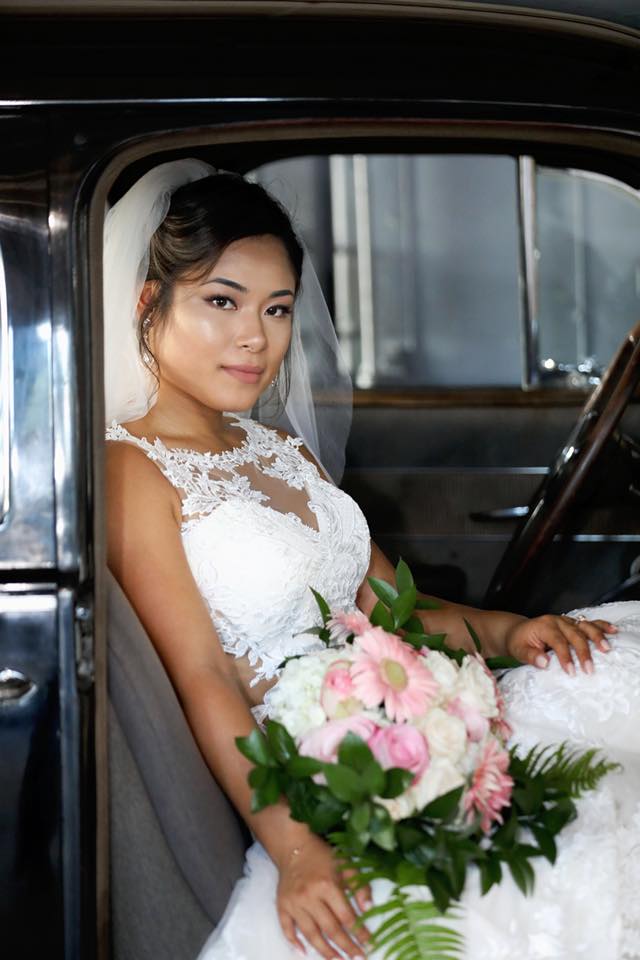 Brunette bride in white wedding dress is sitting inside antique car